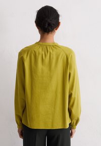 Lange mouwen shirt in olijfgroen, gemaakt van zachte stof, met een geplooide achterkant bij de halslijn en fitted manchetten, gecombineerd met zwarte broeken.