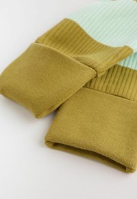 Calcetines tejidos doblados con puños acanalados en colores amarillo mostaza y verde menta claro sobre una superficie blanca.
