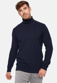 Mørkeblå høyhalset genser med en teksturert herringbone-mønster, ribbestrikkede mansjetter og kant, laget av mykt strikket stoff.