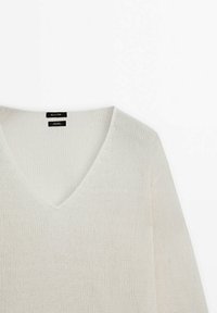 Jasnobeżowy sweter z dekoltem w serek, wykonany z teksturowanej dzianiny, z długimi rękawami i prostym wzornictwem. Metka widoczna przy dekolcie.