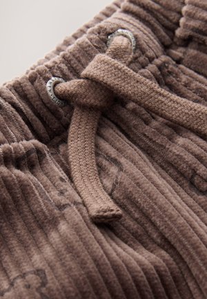 Brązowa tkanina sztruksowa z pionowymi prążkami, wyposażona w pleciony sznurek oraz metalowe oczka do regulacji. Widoczne szczegóły tekstury powierzchni.