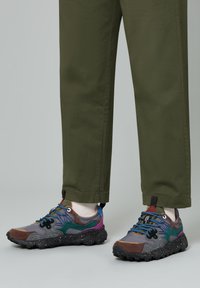 Baskets multicolores avec un mélange de gris, marron et accents teal, dotées d'une semelle texturée, de lacets contrastés et d'une semelle intermédiaire mouchetée.
