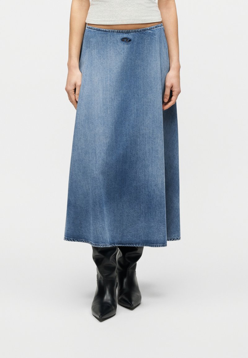 Μπλε τζιν φούστα μέσης μήκους με ελαφρά φούστα, φορεμένη με μαύρα μποτάκια με μυτερή μύτη, εμφανιζόμενη από τη μέση έως τα πόδια σε λευκό φόντο.