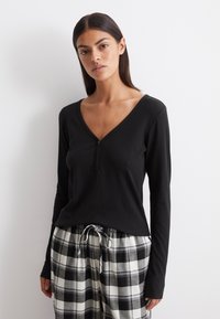Zwarte lang mouwen top met een V-hals en knoopsluiting, gecombineerd met pyjamabroek in zwart-wit geruit patroon met een elastische tailleband.