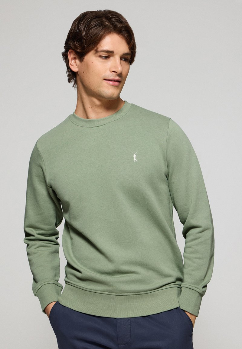 Grön sweatshirt i mjukt bomullsmaterial, med rundad hals, ribbade muddar och en liten vit logotyp på bröstet.