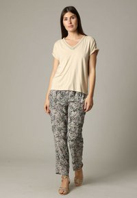 T-shirt beige à manches courtes et col en V, associé à un pantalon à motifs multicolores avec une texture douce et des accents subtils.