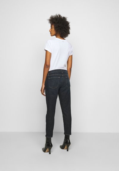 T-shirt bianco a maniche corte abbinato a jeans slim-fit blu scuro e stivali neri con tacco alto, visto da dietro.