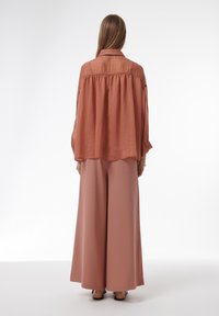 Lange, loszittende rooskleurige blouse met kraag en elastische achterkant, gecombineerd met wijde broekspijpen in een bijpassende tint. Gladde stof textuur.