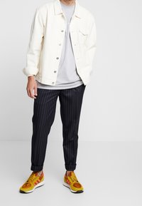 Vit denimjacka över en grå t-shirt, parat med svarta linjerade byxor och färgglada sneakers med inslag av gult, orange och rosa.