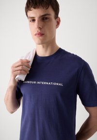 Tricou din bumbac bleu marin cu logo-ul alb "BARBOUR INTERNATIONAL". Mâneci scurte, cu un guler clasic rotund, textură netedă.