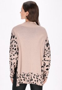 Beige pulóver fekete leopárdmintával a hüvelyeken és az alsó szegélyen, bordás gallérral és laza szabással. Puha textúra és könnyű anyag.
