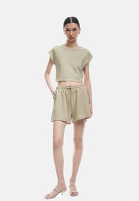 Top corto in cotone a costine color khaki e pantaloni abbinati con vita elasticizzata e cordino. Modello in piedi con le mani nelle tasche. Vestibilità slim.