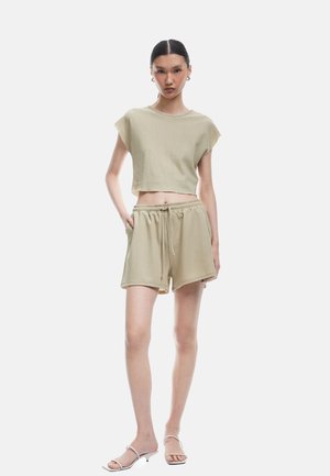 Kaki ribbet bomulds cropped top og matchende shorts med elastisk talje og snøre. Modellen står med hænderne i lommerne. Slank pasform.
