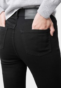 Jeans de mezclilla negra con corte ajustado, que cuentan con bolsillos traseros y una etiqueta de cuero con la inscripción "AUTOGRAPH". La tela tiene una textura suave.
