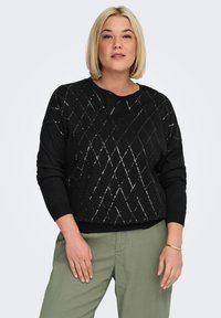 Black knitted sweater with a diamond pattern in silver threads, round neckline, and long sleeves; paired with light green trousers.