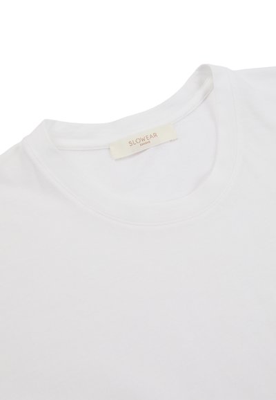 Camiseta de cuello redondo blanca con una etiqueta cosida que dice "SLOWEAR 24/ZONE" visible dentro del cuello.