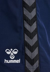 Granatowy top sportowy z pionowym pasem w czarno-białe zygzaki oraz białym logo z motywem pszczoły w lewym dolnym rogu.