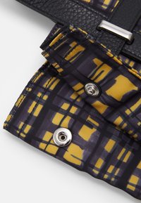 Matériau noir texturé avec un tissu à motifs jaune et violet. Comprend des éléments en métal argenté et une fermeture à bouton-pression.