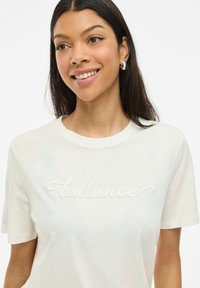 Vit bomull t-shirt med korta ärmar, med upphöjd broderad text "balance" i kursiv stil på framsidan.
