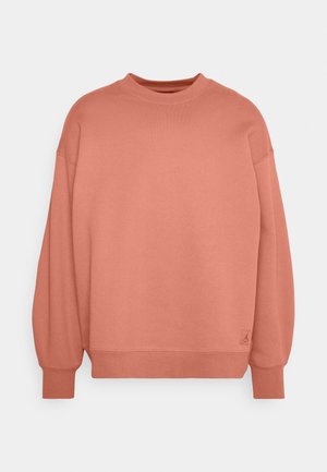 Sudadera de color rosa con cuello redondo, hombros caídos y puños acanalados. Fabricada en suave tejido de algodón con un pequeño parche de logotipo.