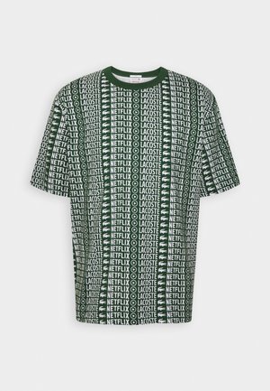 Groen T-shirt met korte mouwen met herhaalde patronen van "NETFLIX" en "LACOSTE" logo's, voorzien van een ronde hals en een losse pasvorm.