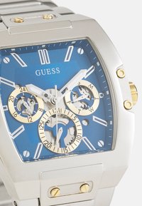Silver stainless steel watch with a square case, blue dial, gold accents, and exposed gears. Features white hour markers and chronograph sub-dials.