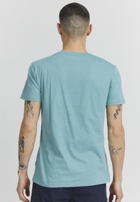 Gaiši zils īsajām piedurknēm T-krekls, izgatavots no mīksta kokvilnas, ar apaļu kakla izgriezumu un taisnu apakšmalu. Muguras dizains ir vienkāršs, bez rotājumiem.