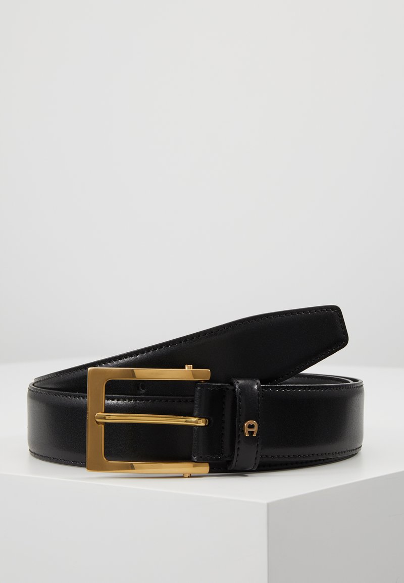 Ceinture en cuir noir avec une boucle rectangulaire en or, présentant une texture lisse et des bords nets. Les accents notables incluent un logo près de la boucle.