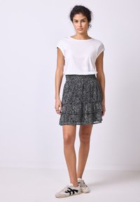 Jupe à motifs noir et blanc avec un design à volants, assortie à un haut blanc uni à manches courtes et des baskets grises.