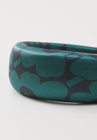 Grønn og svart mønstret armbånd laget av glatt, blankt materiale, med en rund og bred form med blomstermønster.