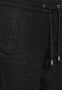 Pantaloni di lino neri con finitura testurizzata, dotati di tasche laterali e vita con cordoncino in contrasto con hardware viola e argento.