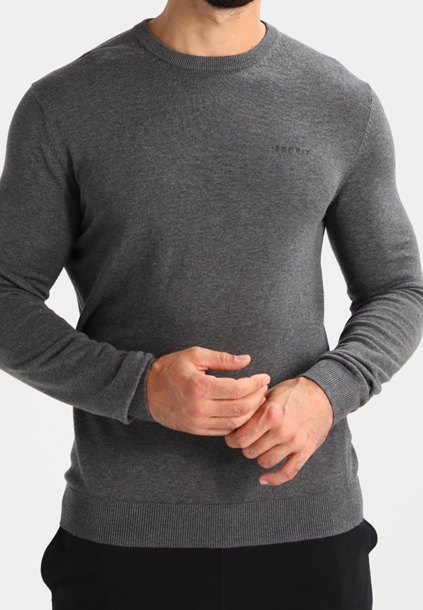 Homme portant un pull ajusté à manches longues gris foncé avec poignets et ourlet côtelés, ajustant les manches avec les deux mains.