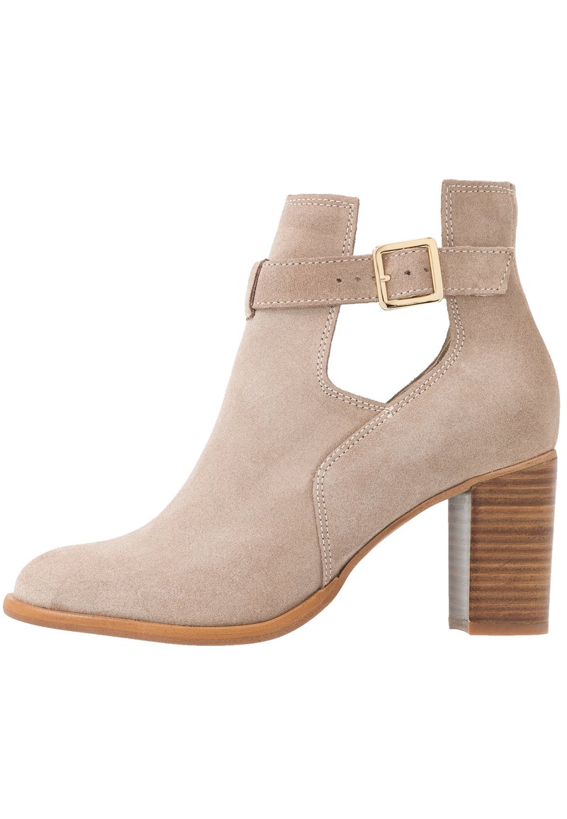 Bottine beige en daim avec talon épais, détail découpé sur le côté et bride réglable avec boucle dorée.