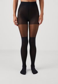 Svarta genomskinliga nylonstrumpor med hög midja, med en strukturerad ovandel och en slät underbendel, som betonar en genomskinlig till midjan-design.