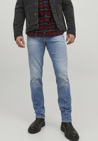 Jeans de denim de culoare albastru deschis, cu un finisaj ușor decolorat, asortați cu o jachetă neagră și o cămașă cu carouri roșii. Bocanci negri la gleznă completează ținuta.