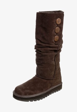 Bruine suède kniehoge laars met een nonchalant ontwerp, voorzien van drie bruine knoppen aan de buitenkant en een rubberen zool. Getextureerde afwerking.