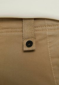 Khaki tkanina s tkaným popruhem a detailně černým knoflíkem, s viditelným švem a hladkou texturou. Obrázek je zblízka.
