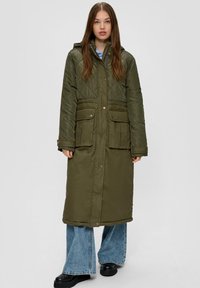 Lange, gewatteerde, olijfgroene jas met een capuchon, met twee voorzakken en drukknoopsluitingen, gecombineerd met wijde denim jeans.