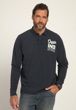Mørkeblå langærmet polo-t-shirt med krave, to knapper og trykt tekstdesign på brystet. Båret sammen med blå denim-jeans.