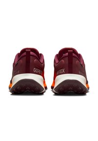 Une paire de chaussures de course Gore-Tex maroon et orange vue de l'arrière, mettant en avant les semelles texturées et les languettes au niveau du talon.