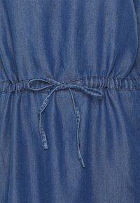 Denim-vaate syvän sinisena, jossa on kerätty elastinen vyötärö ja kangasnaru säätämistä varten. Sujuva pinta, rento muotoilu.