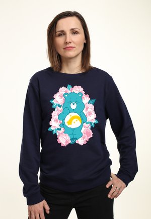 Marineblå sweatshirt med et blåt bjørnegrafik omgivet af lyserøde roser, med et regnbue-design på bjørnens mave. Blødt, afslappet stof.