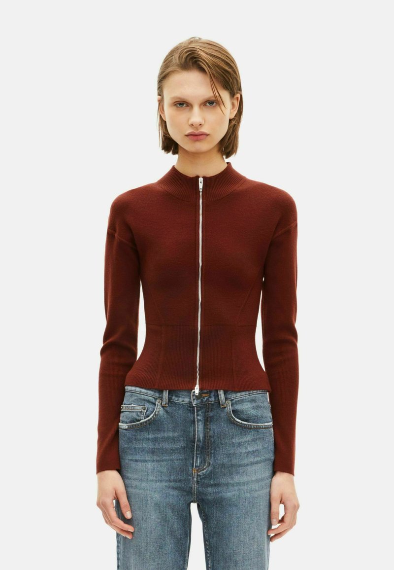 Maglione zip-up borgogna con texture a coste e design aderente, caratterizzato da maniche lunghe e colletto alto, abbinato a jeans blu.