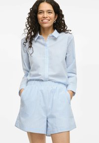 Chemise bleue clair à boutons avec des rayures blanches verticales, associée à un short à taille élastique assorti, comportant des poches latérales.