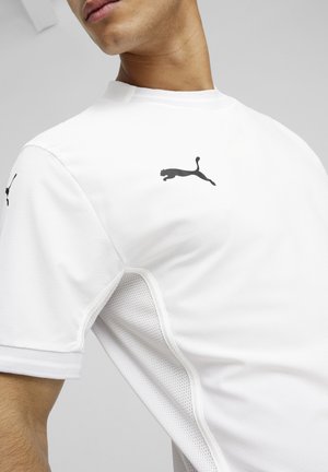Witte sportshirt met zwart Puma-logo op de schouder. Heeft geperforeerde meshpanelen aan de zijkanten voor ademend vermogen. Korte mouwen, ronde hals.