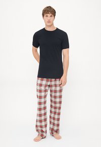 Schwarzes kurzärmeliges T-Shirt, kombiniert mit rot, weiß und schwarz karierten Hosen; die Hose hat einen elastischen Bund und einen lockeren Schnitt.