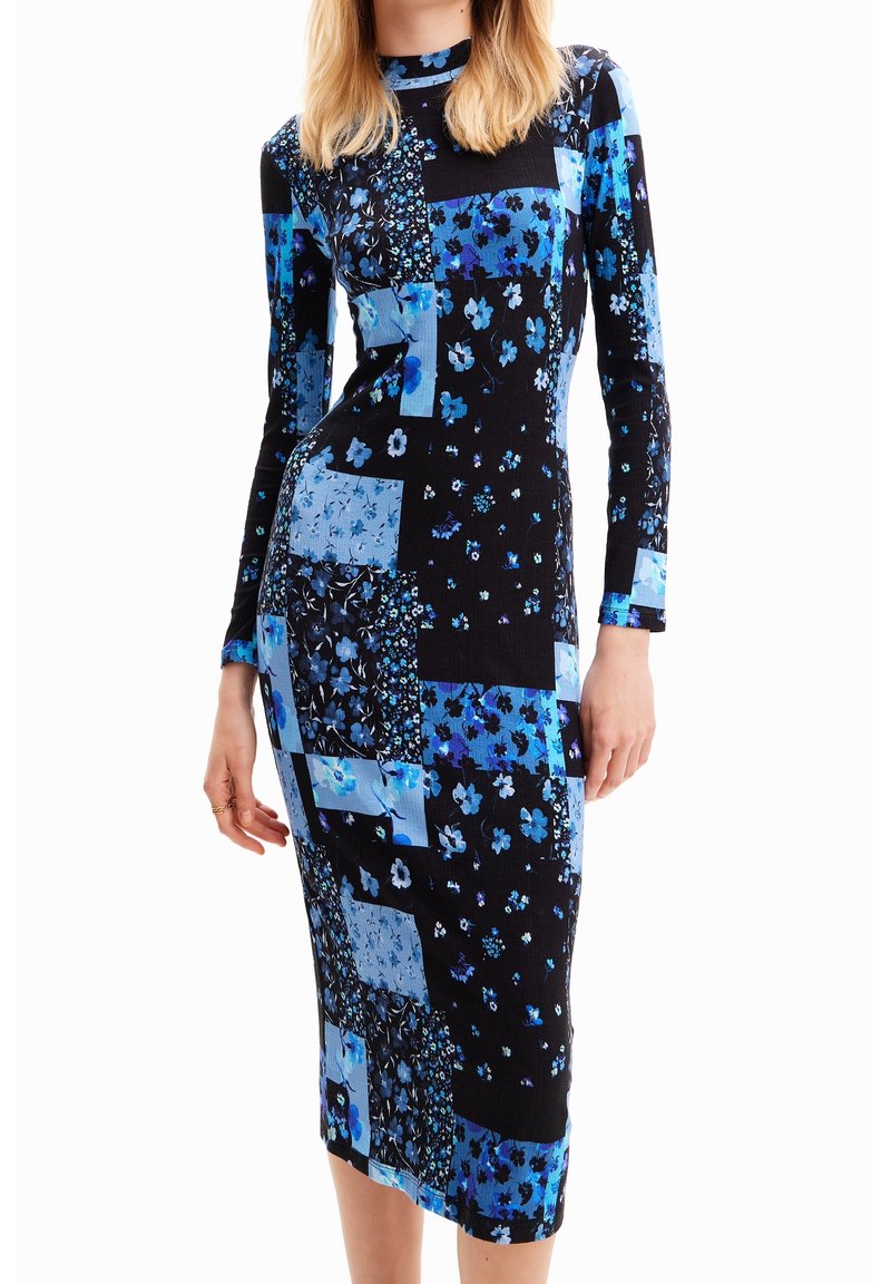 Femme portant une robe midi ajustée à manches longues avec un motif patchwork de fleurs bleues et noires.