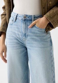 Jasnoniebieskie dżinsy z denimu o wysokim stanie, prostym kroju nogawek i delikatnym wyblaknięciu. Posiadają zapięcie na guzik oraz boczne kieszenie.