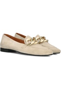 Beige suède loafers met een decoratieve gouden ketting aan de voorkant, een puntige neus en een platte zwarte rubberen zool.