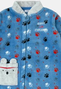 Bata de forro polar en azul claro con estampados multicolores de huellas. Con texto bordado "FELIZ pequeño EXPLORADOR" y un bolsillo en forma de oso.